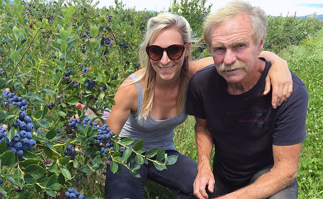 Man and woman kneeling in a row of blueberry bushes